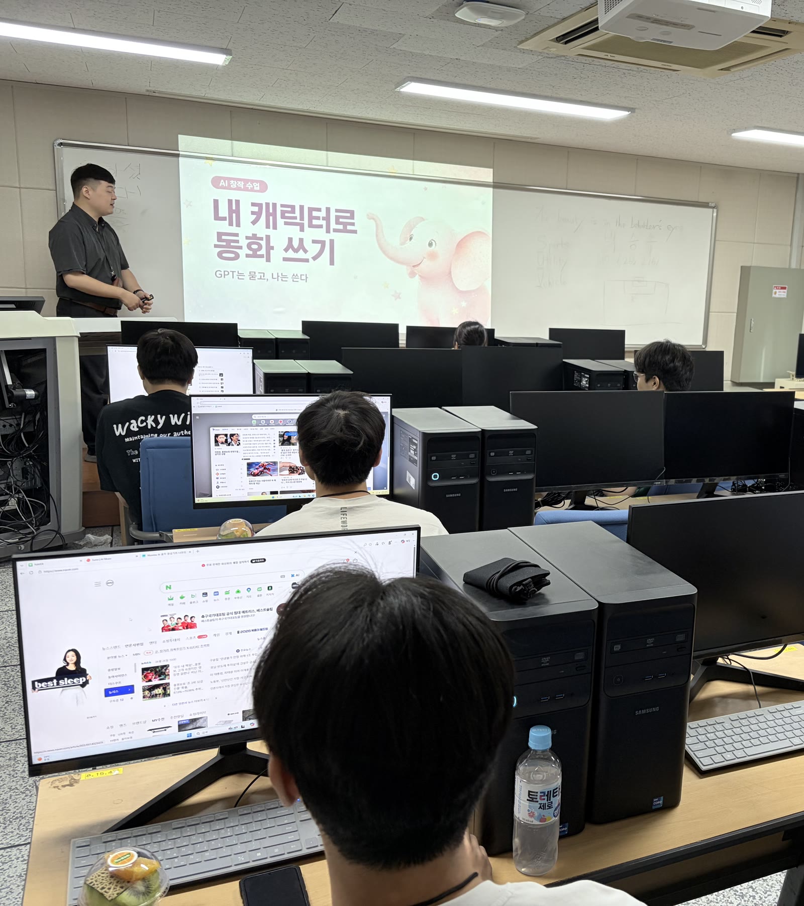 AI 창작 수업 '내 캐릭터로 동화 쓰기' — 원장이 분홍 코끼리 화면 앞에서 강의하고 수강생들이 화면을 보고 있습니다